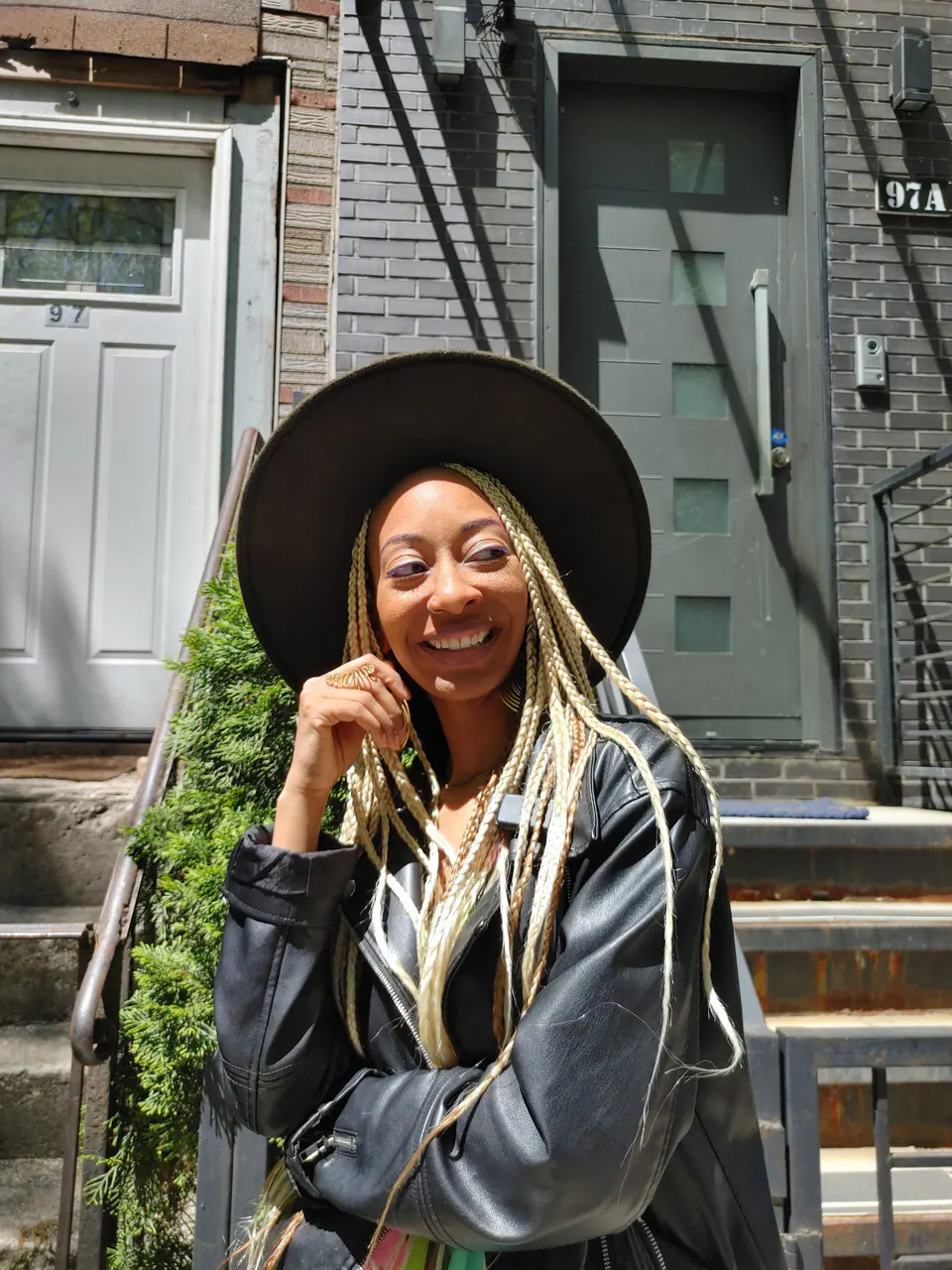 Donna Marie smiling on brownstone stairs in a wide-brim hat and leather jacket