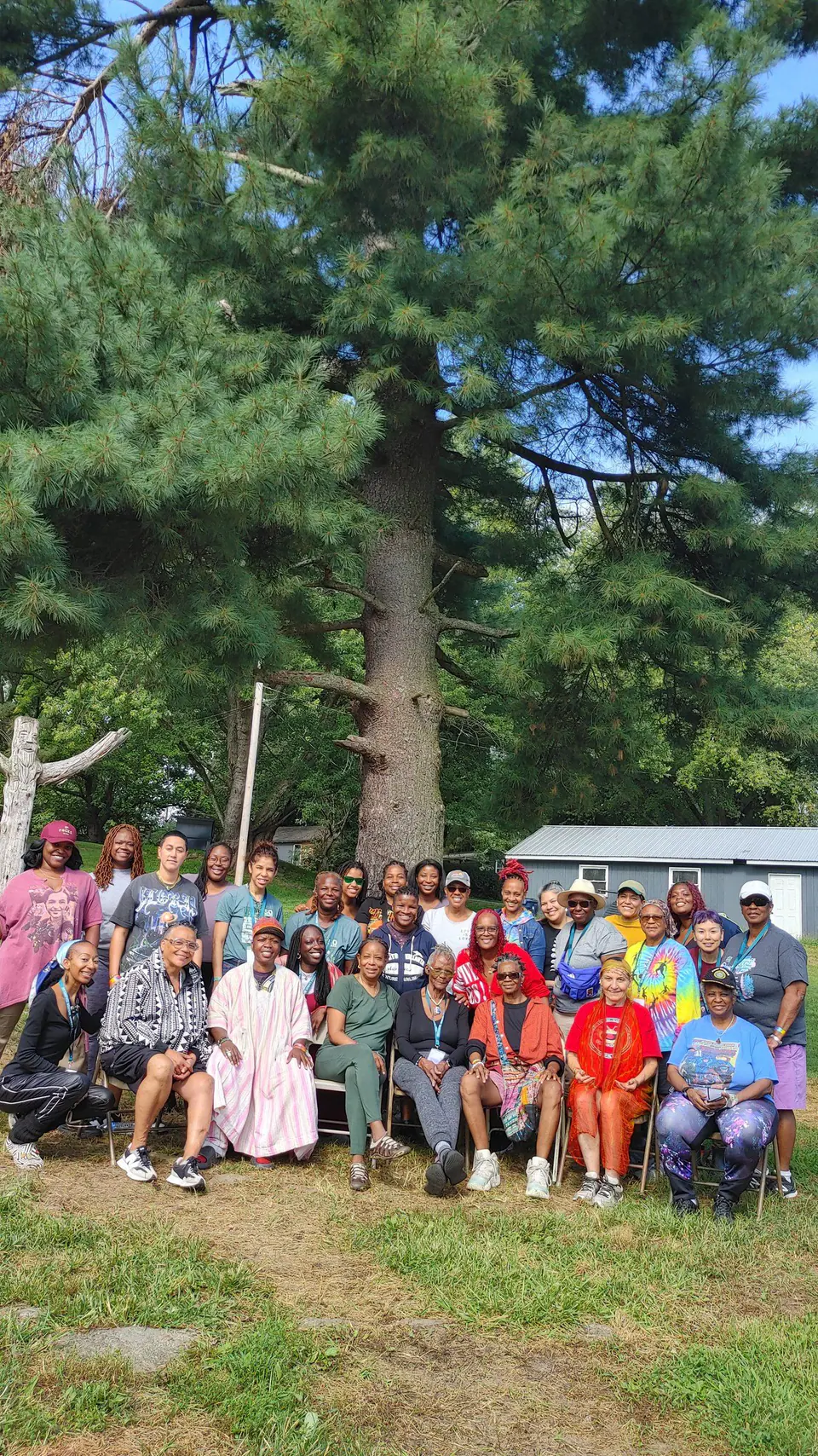 A large smiling group gathered outdoors under tall trees