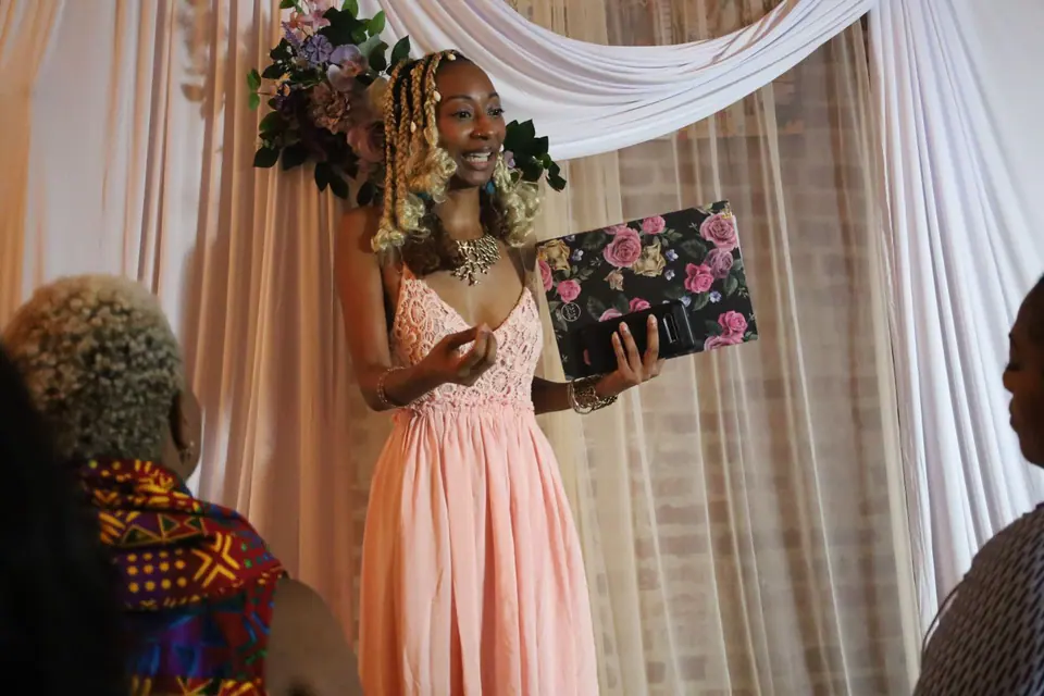Donna Marie speaking to the room, holding a floral clutch