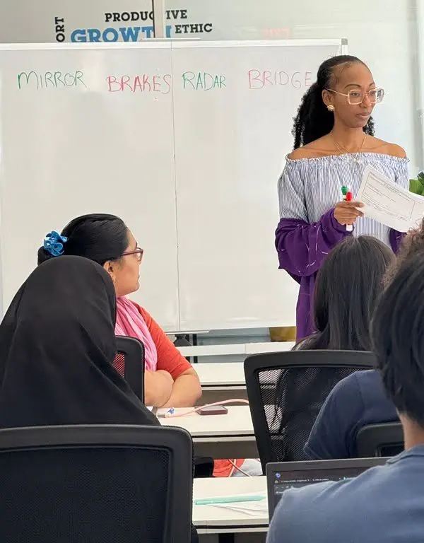 Donna Marie teaching a classroom of young adults, standing in front of a whiteboard that reads Mirror, Brakes, Radar, Bridge